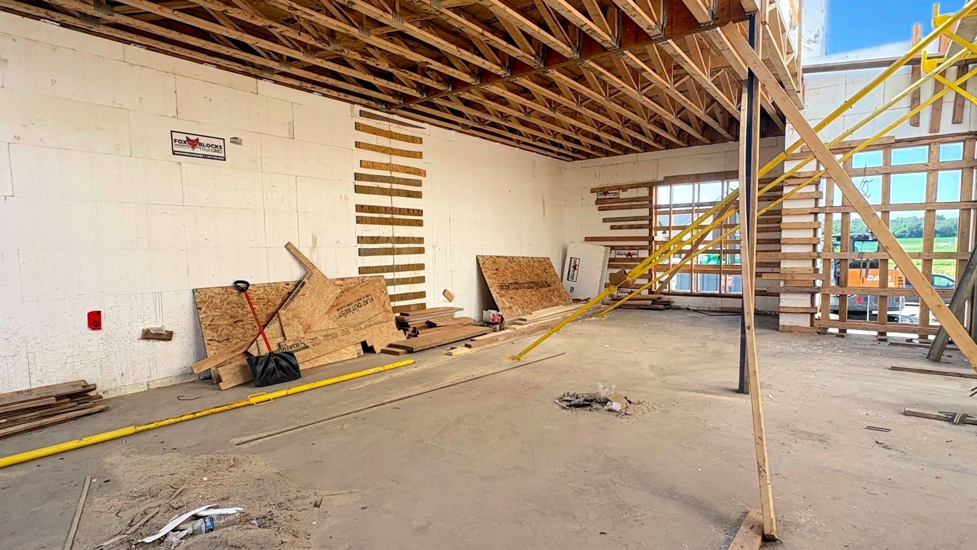 Interior of a building under construction, with exposed wooden beams, concrete floor, and scaffolding.