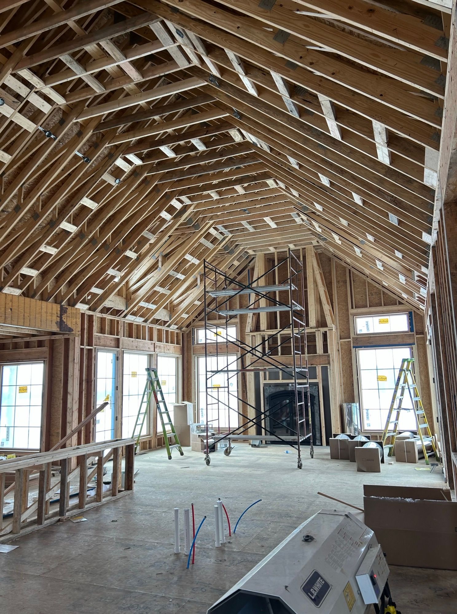 Interior of a house under construction. Exposed wooden beams form the roof and walls; windows and a fireplace are visible.