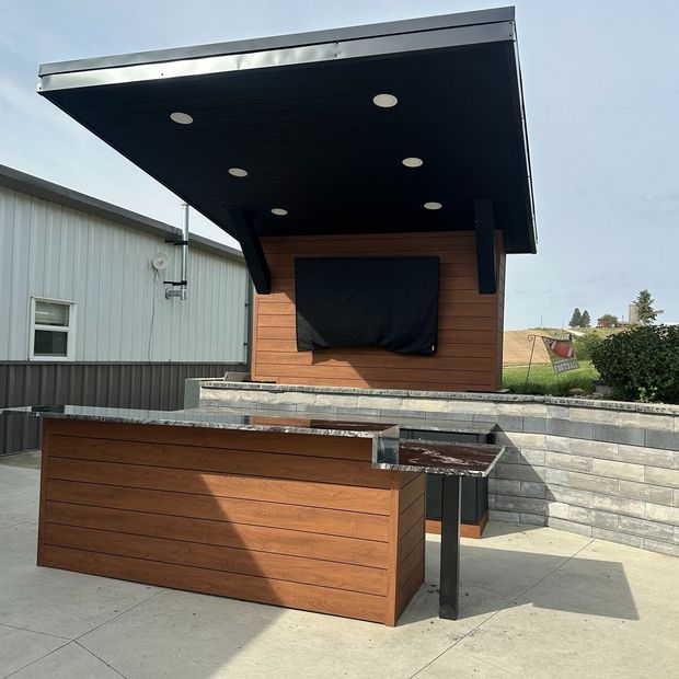Outdoor bar with a TV, wood siding, and black roof overhang.
