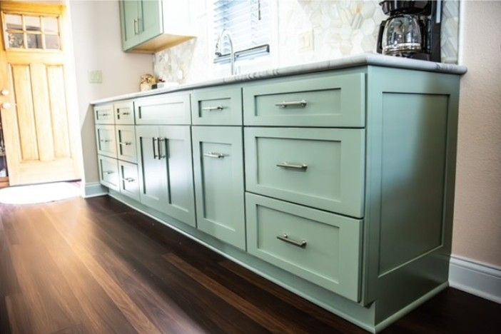Mint-green kitchen cabinets along a dark wood floor in a bright room