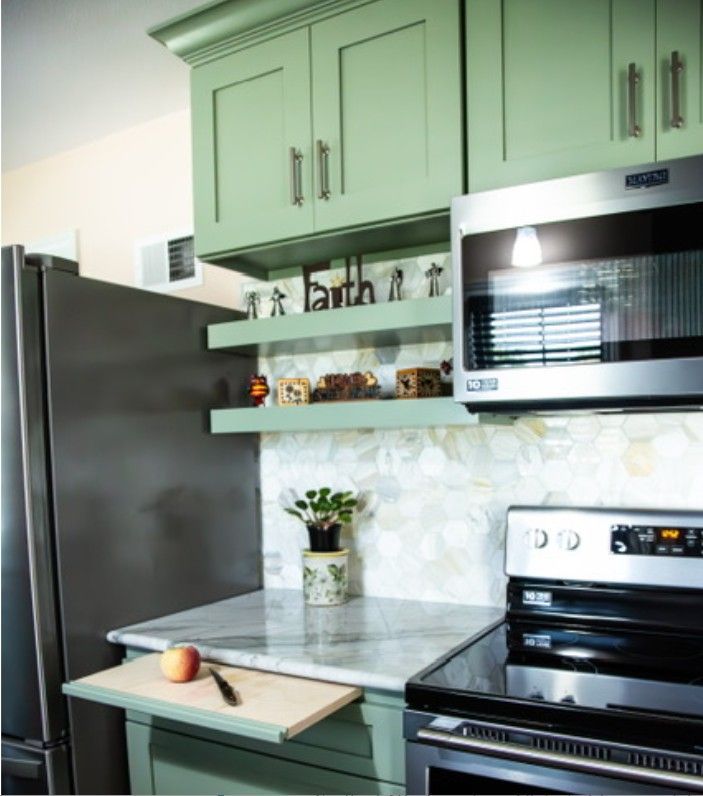 Modern kitchen with mint-green cabinets, stainless steel appliances, marble counter, and floating shelves