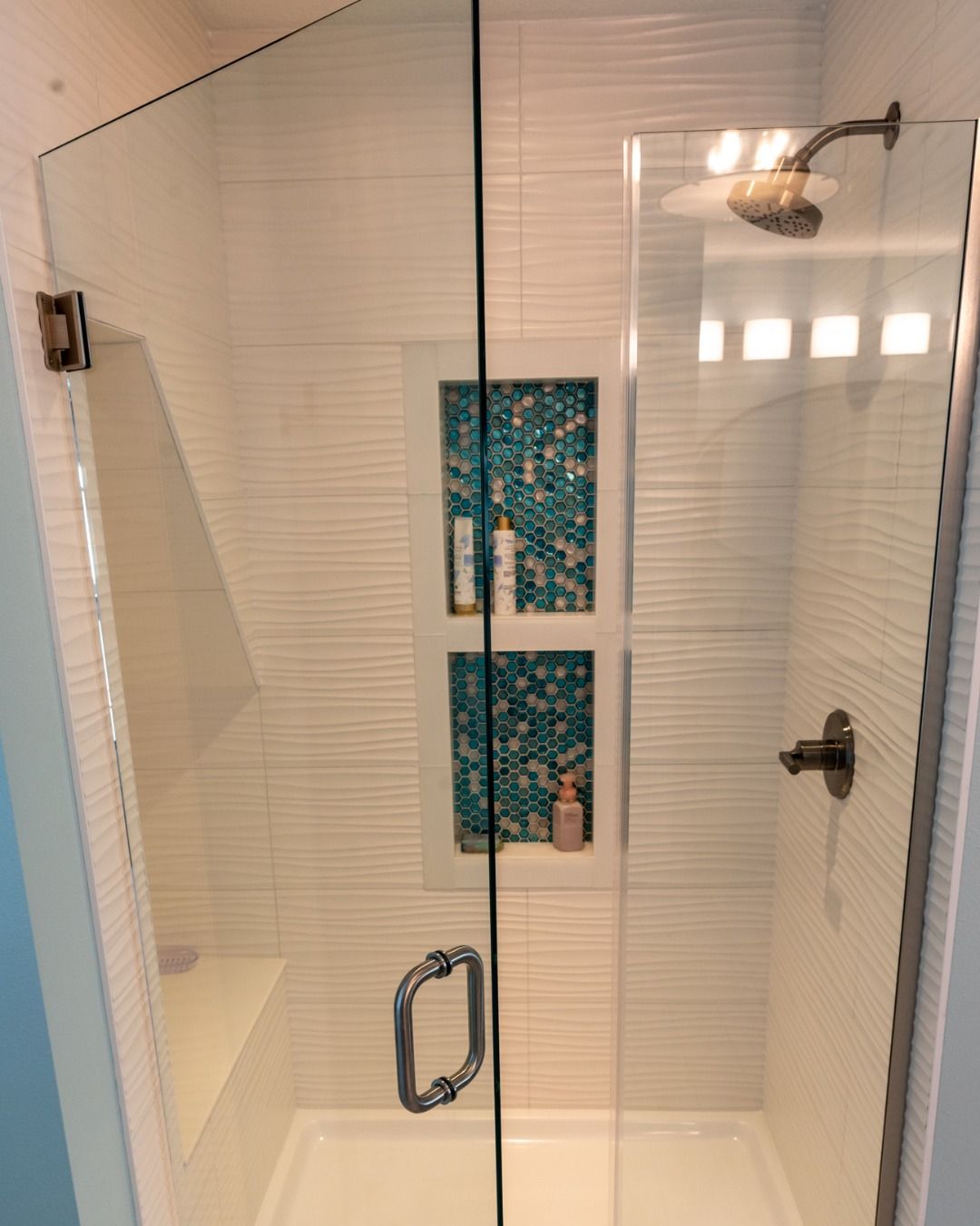 Glass shower enclosure with white tile and turquoise accent shelves.