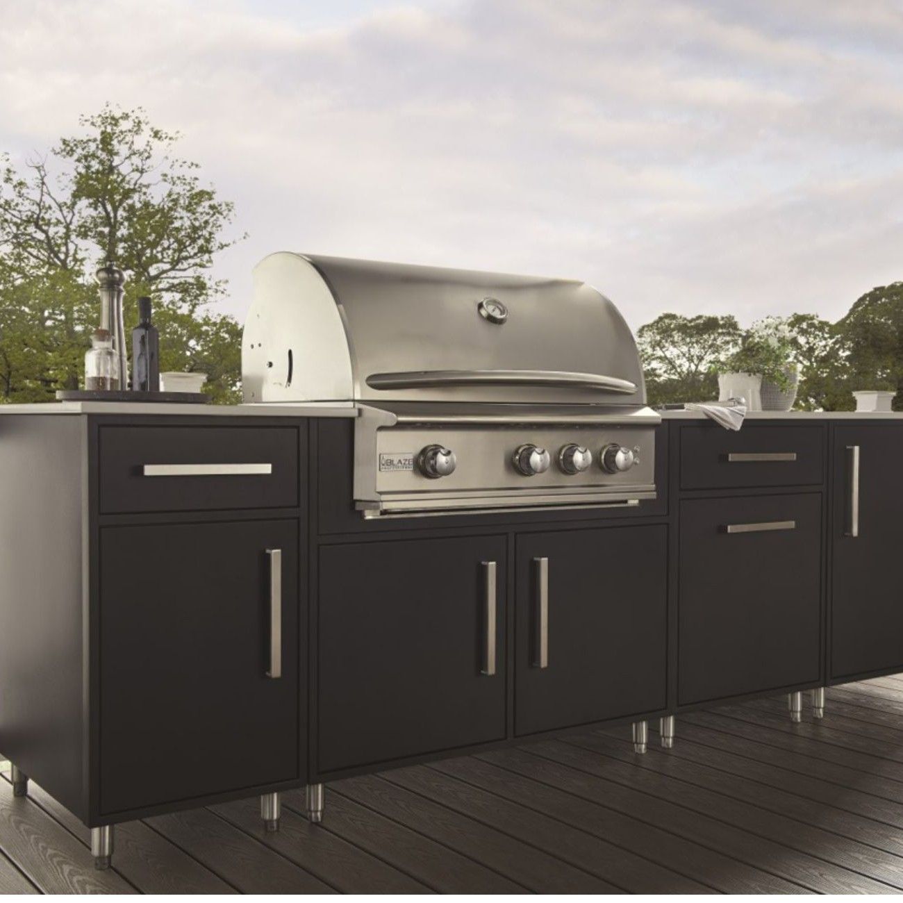 Outdoor black grill with stainless steel hood and cabinets, set on a wooden deck.