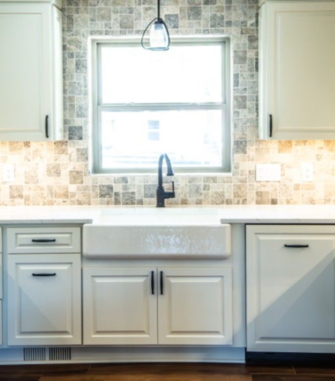 Modern kitchen sink under a window, with white cabinets, gray countertops, and mosaic tile backsplash