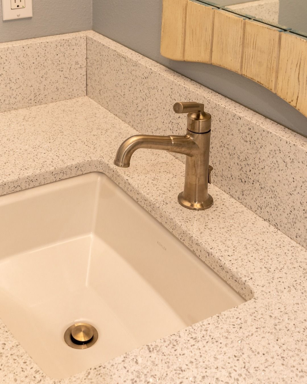 Bathroom sink with gold faucet, set in a white speckled countertop.