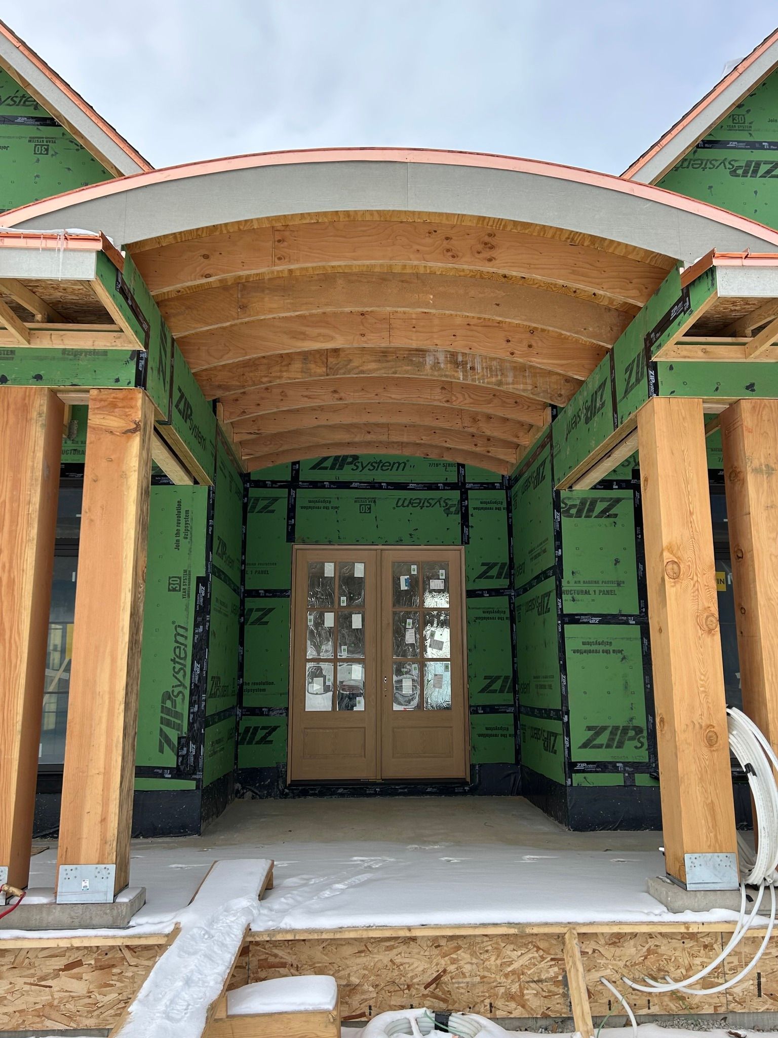 Unfinished home entrance with wood supports and a curved ceiling; double doors visible within.