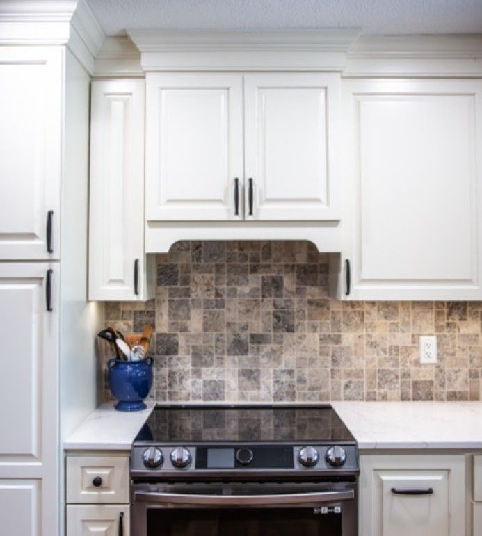 White kitchen with stainless stove, white cabinets, and tan tile backsplash