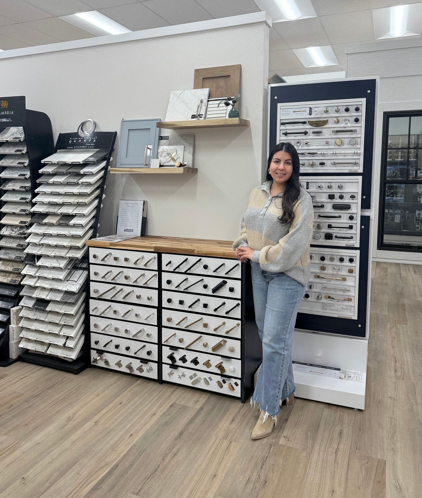 Woman in a showroom stands next to a display of cabinet hardware. Cabinets and samples are visible.