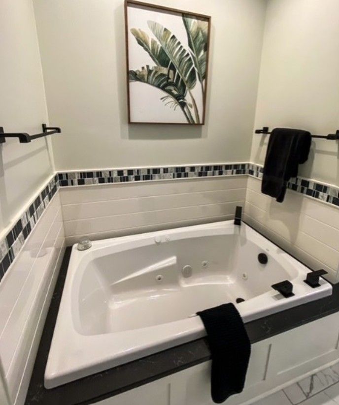 Clean white bathroom with a built-in soaking tub, black fixtures, and a framed leaf print above the tub