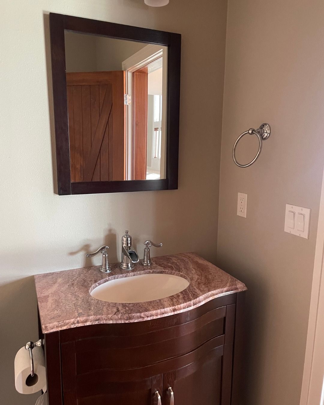 Bathroom with dark wood vanity, pink countertop, mirror, and towel ring on beige walls.