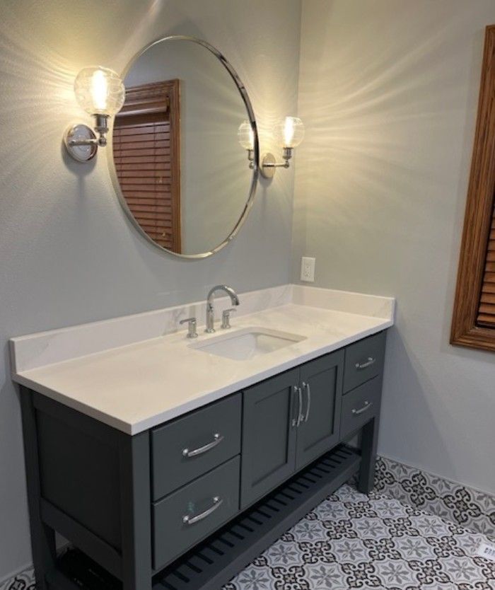 Bathroom vanity with round mirror, wall sconces, and gray cabinet under a white countertop