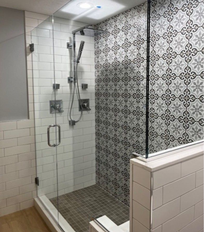 Modern walk-in shower with glass walls, white tile, and patterned gray accent wall