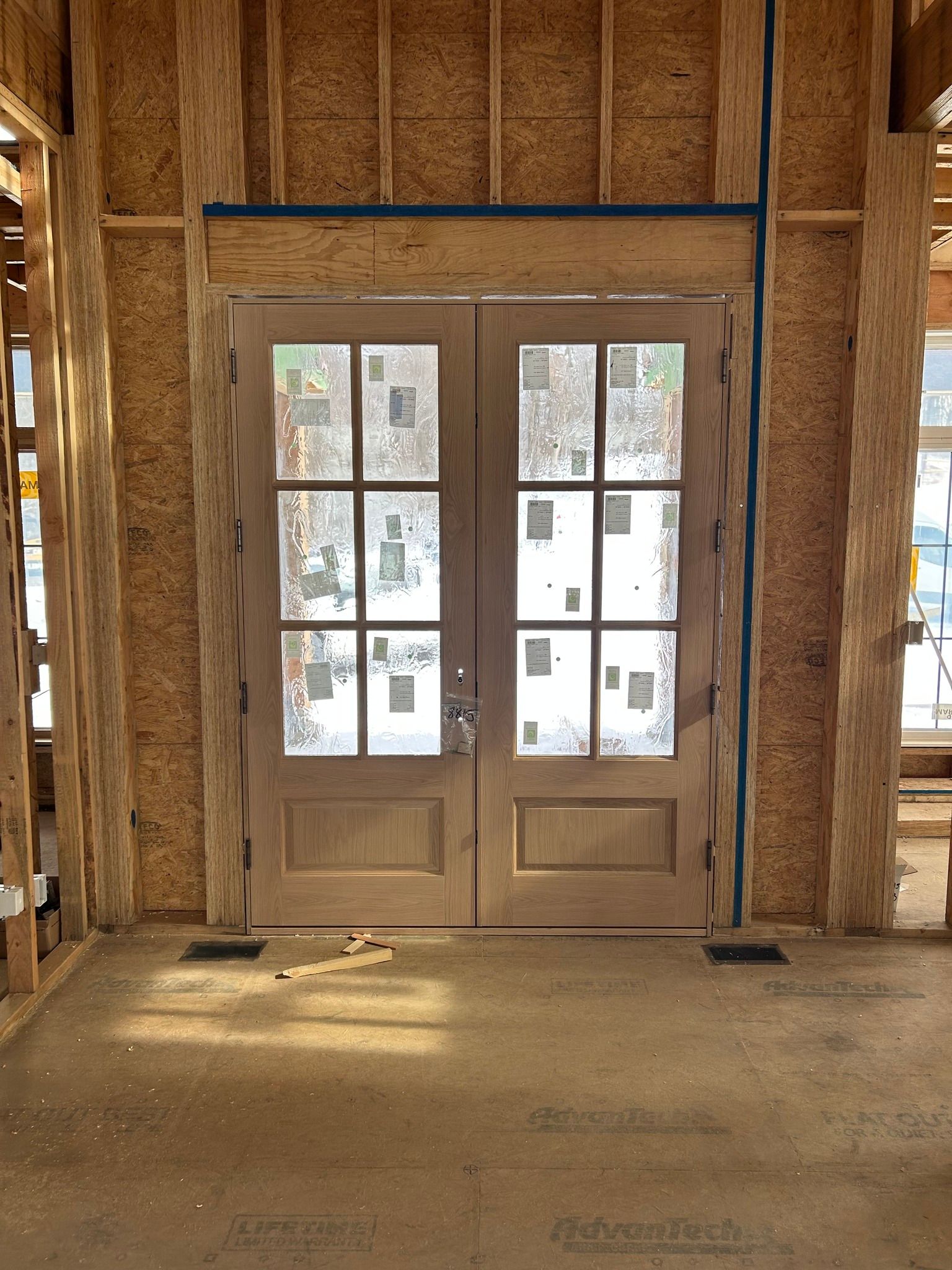 Double wooden doors in unfinished room, windows covered in paper, construction setting.