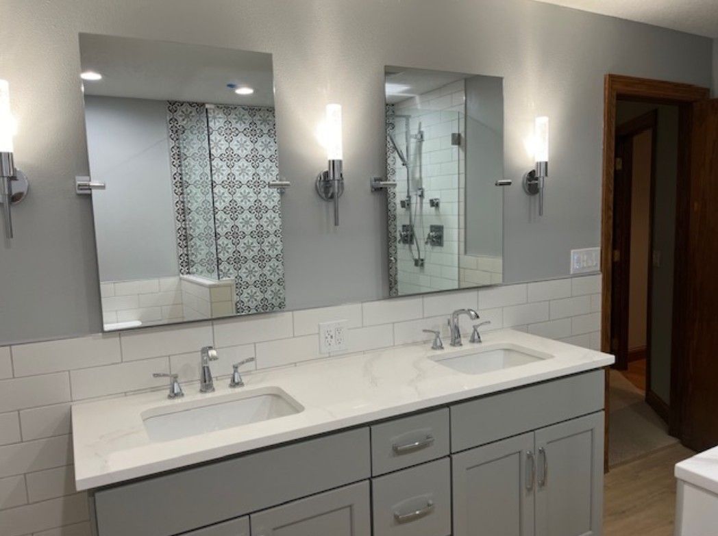 Modern bathroom vanity with double sinks, mirrors, wall sconces, and a gray cabinet beneath a white countertop