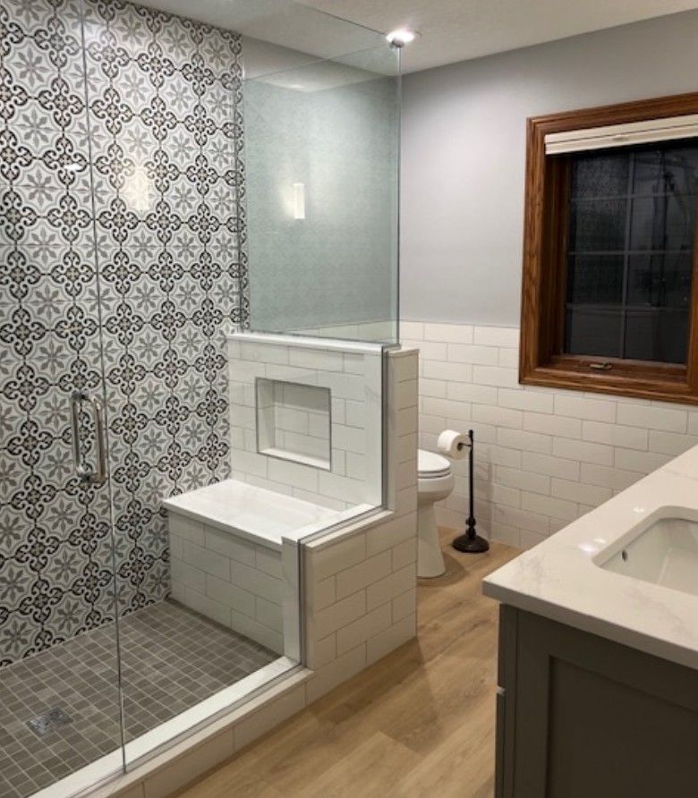 Modern bathroom with tiled shower, built-in bench, wood floor, and window