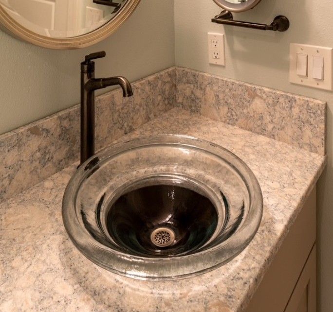 Bathroom vanity with a round black vessel sink, matte black faucet, and beige granite countertop