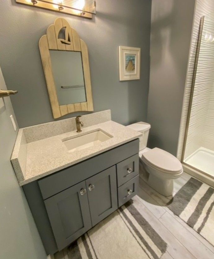 Small gray bathroom vanity with mirror, toilet, shower, and striped rug in a modern room