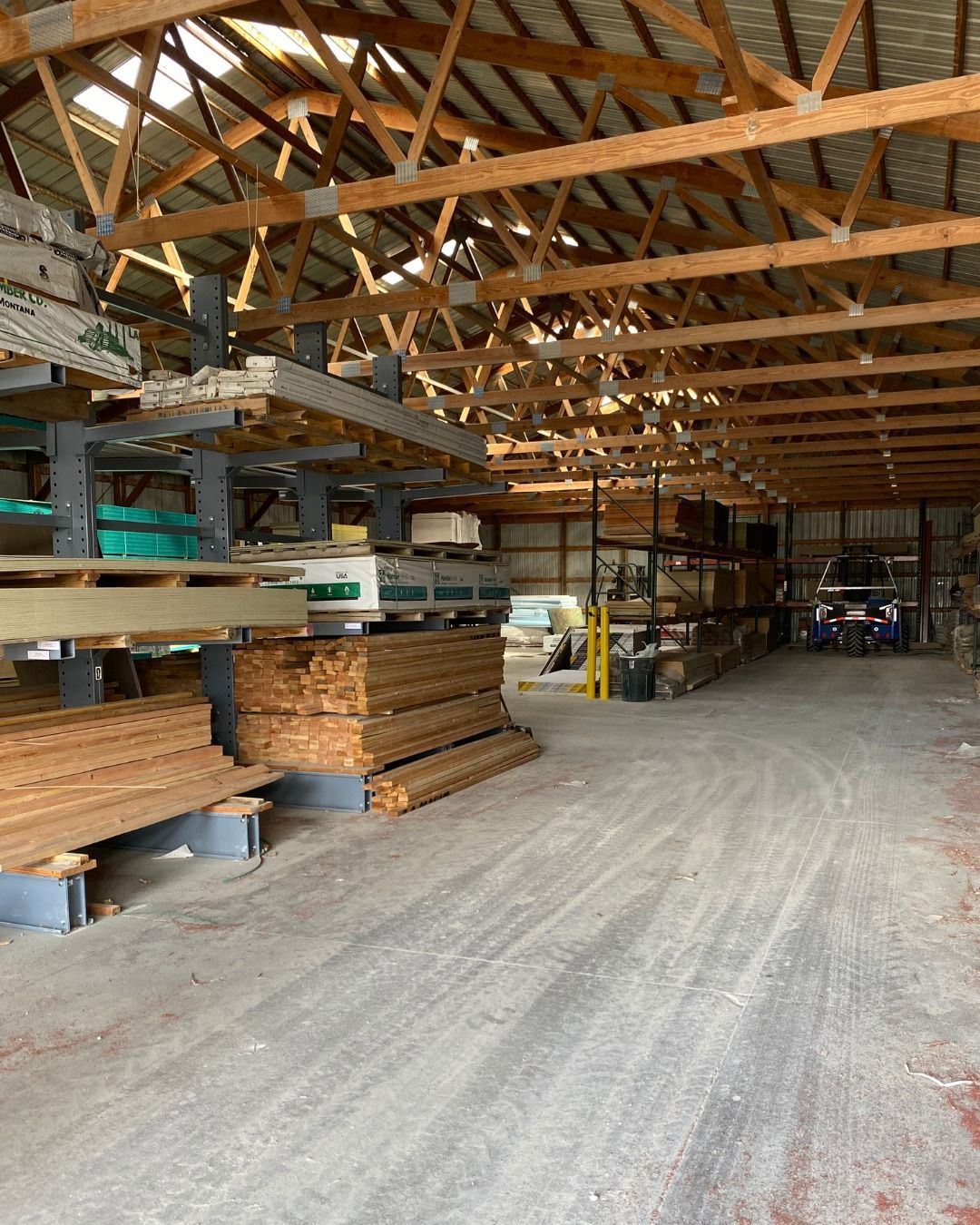 Warehouse interior with wooden beams, storage shelves of lumber, and a vehicle.