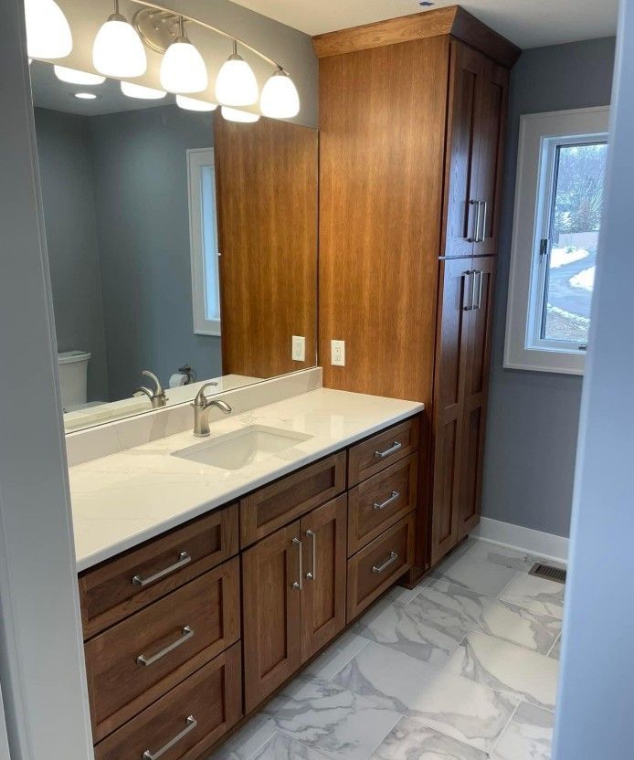 Modern bathroom vanity with wood cabinets, white countertop, large mirror, and marble-pattern tile floor