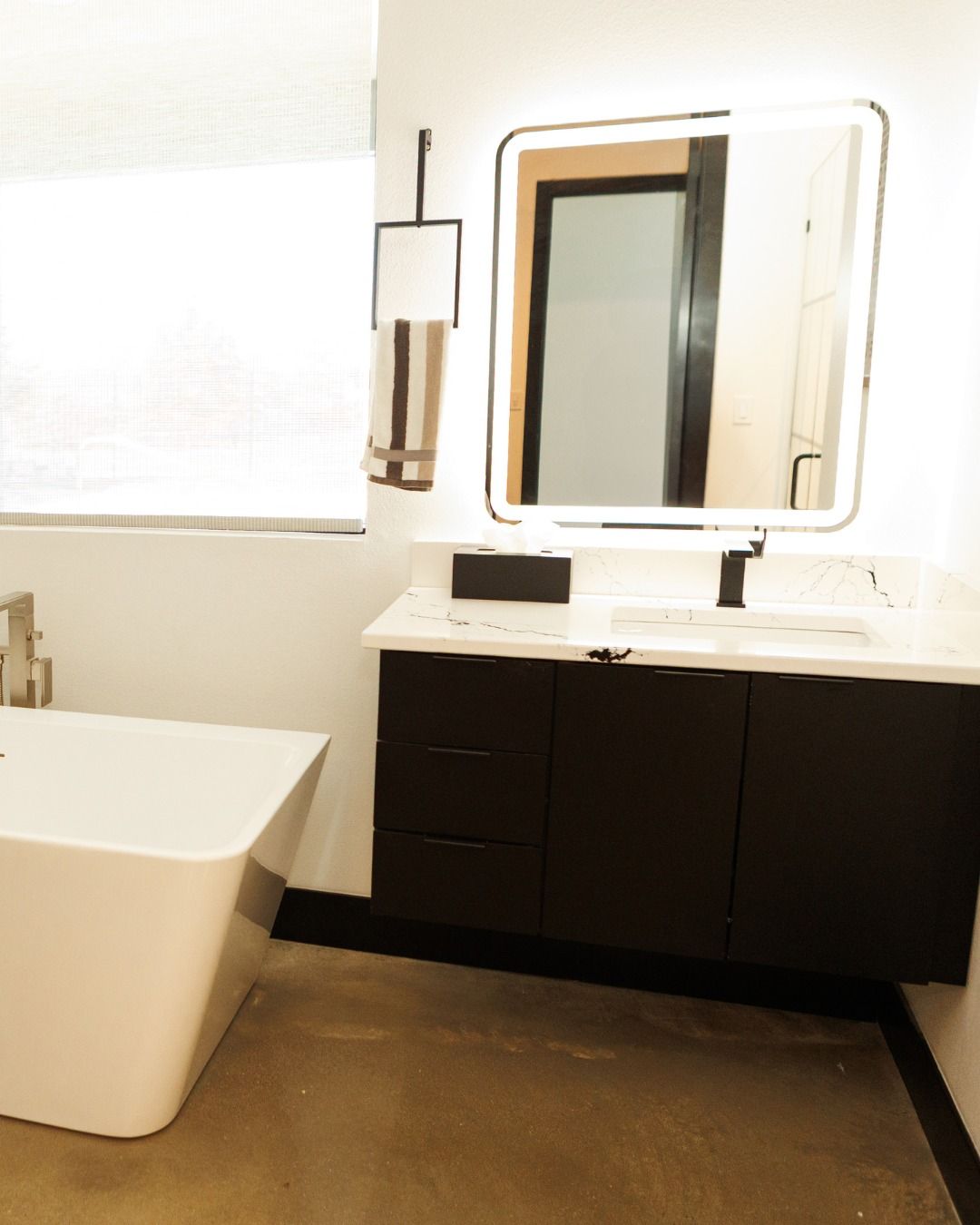 Modern bathroom with black vanity, illuminated mirror, and a white bathtub.