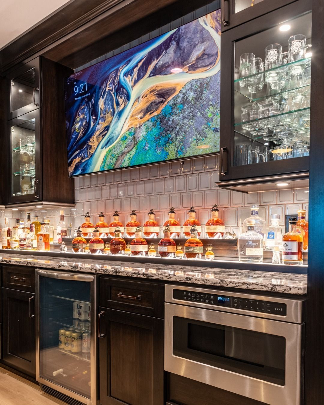 Wet bar with liquor bottles, glassware, and a microwave oven. A colorful abstract painting hangs above.