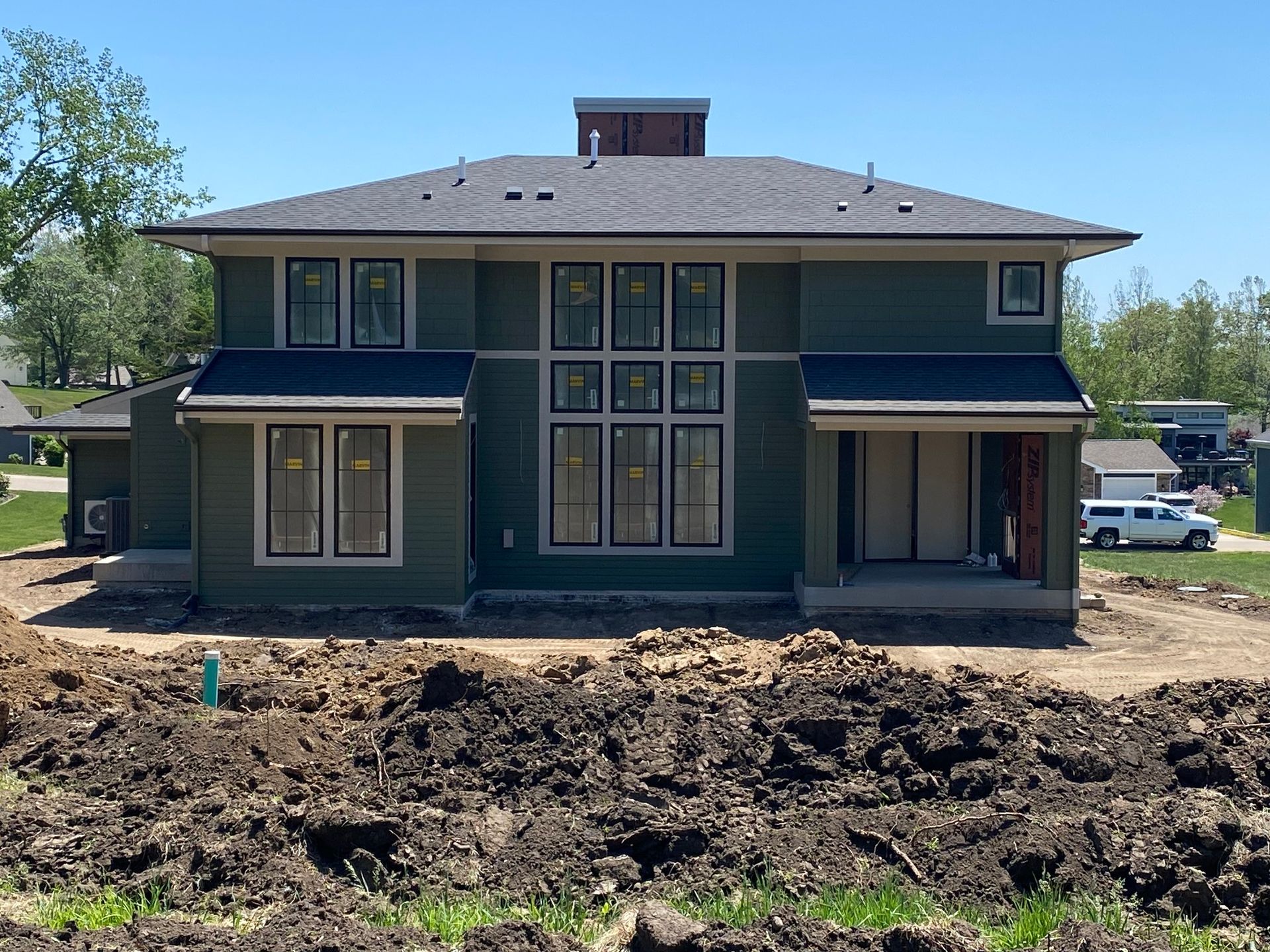 Green two-story house with dark roof and large windows under construction. Brown dirt in the foreground.