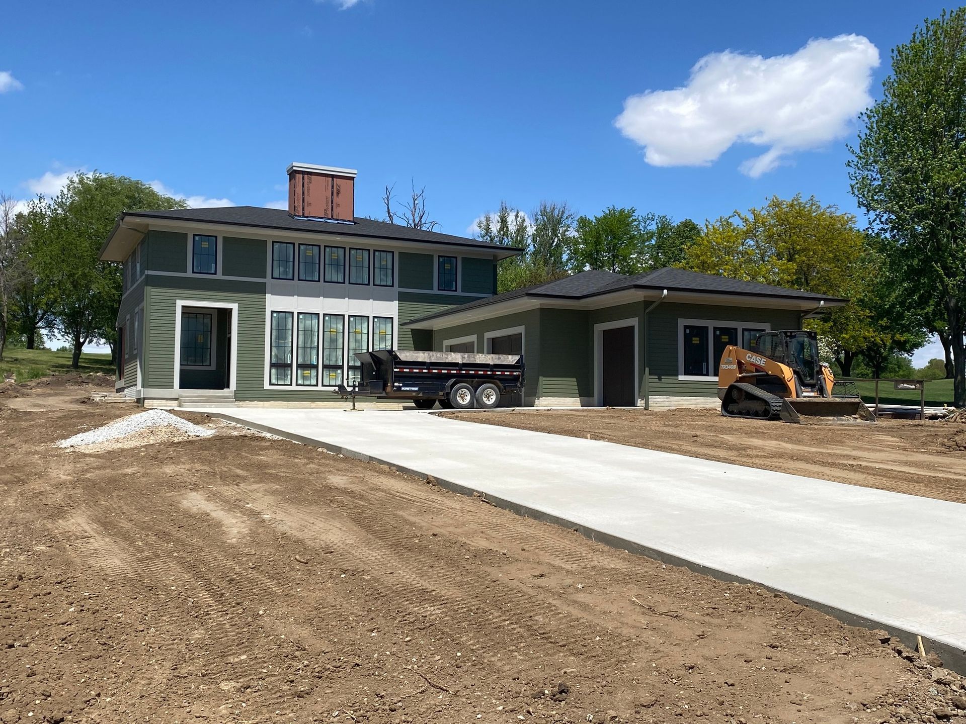 A green, two-story house under construction with a new concrete driveway and a piece of heavy machinery parked nearby.