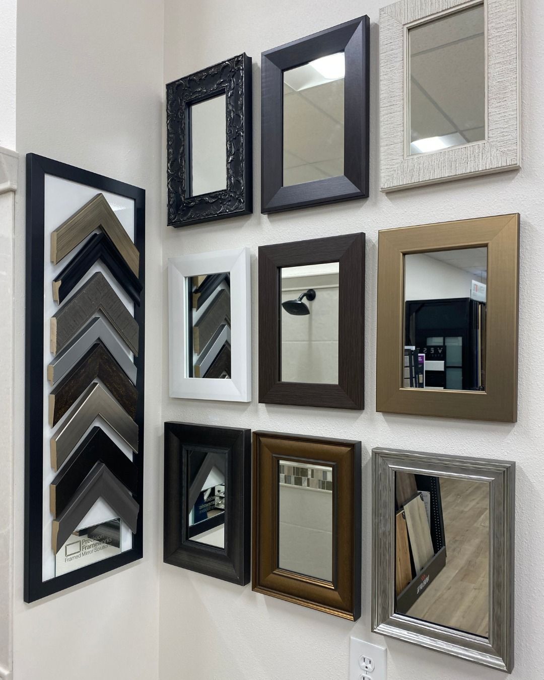 Display of framed mirrors and frame samples on a white wall in a showroom.