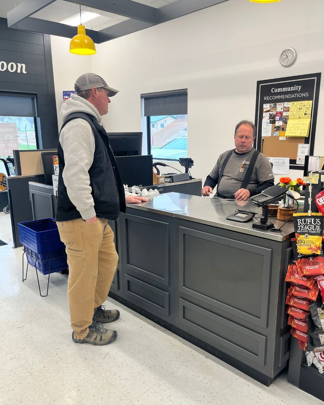 Man standing at a checkout counter, speaking to a cashier in a store.