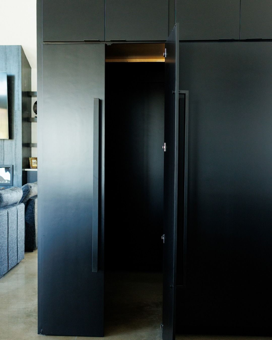 Black closet doors, one partially open, revealing a dark interior. Modern design, minimalist handles.