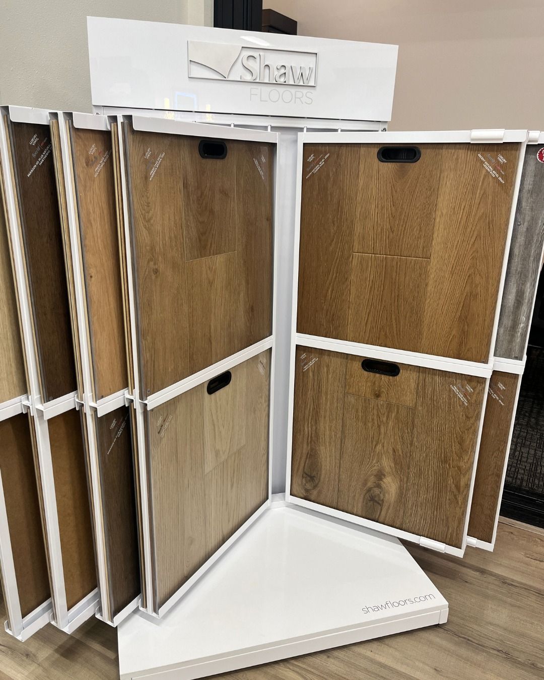 A rotating Shaw flooring display with various wood samples in a showroom.