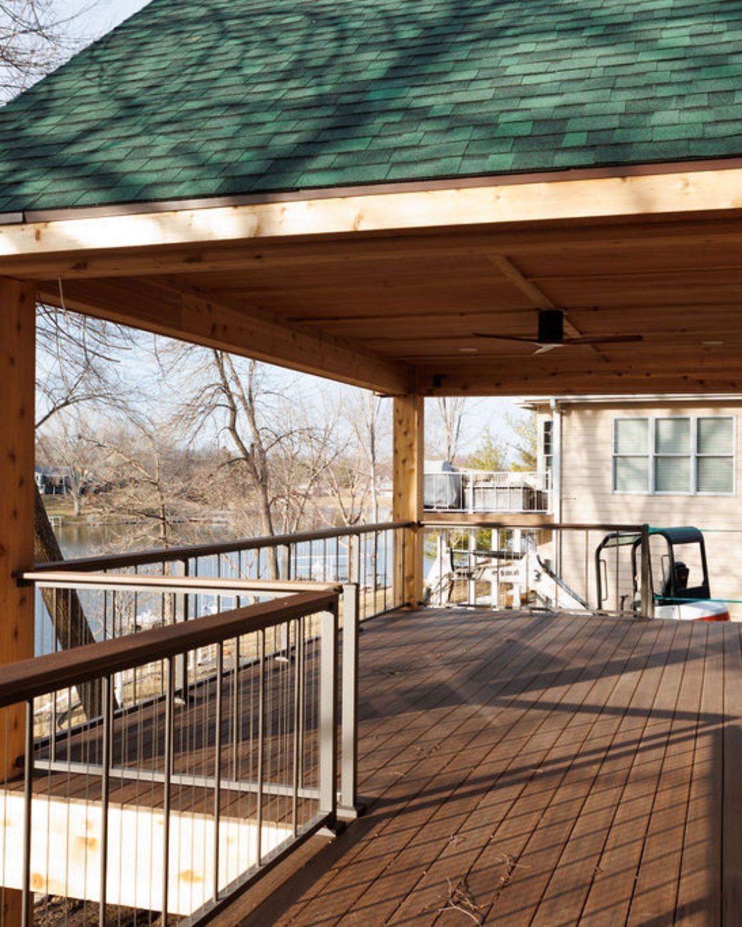 Wooden deck with roof overlooking a river, with metal railings. Sunny day.