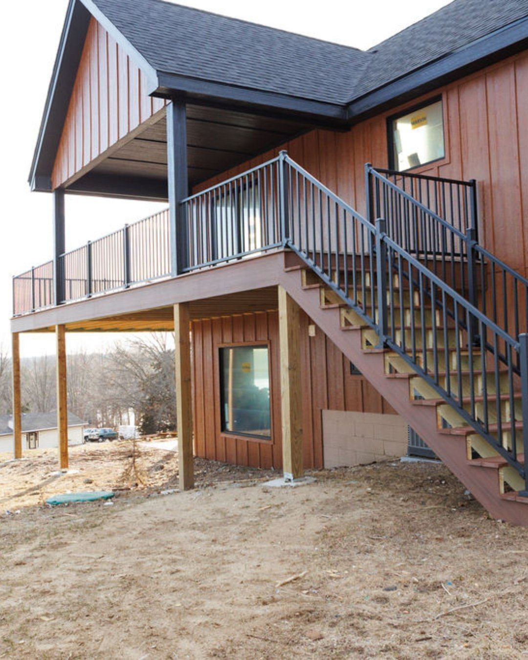 Brown two-story house with a deck and stairs. Exterior is brown siding and black railings.
