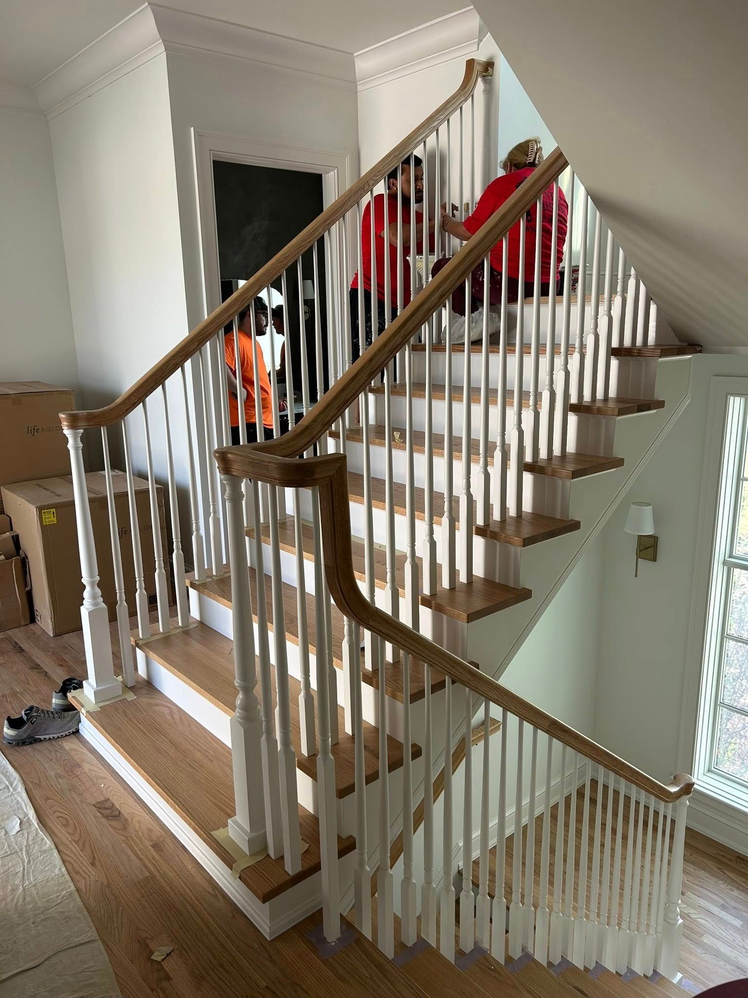 Staircase with light wood steps, white balusters, and two people in red shirts on the landing.