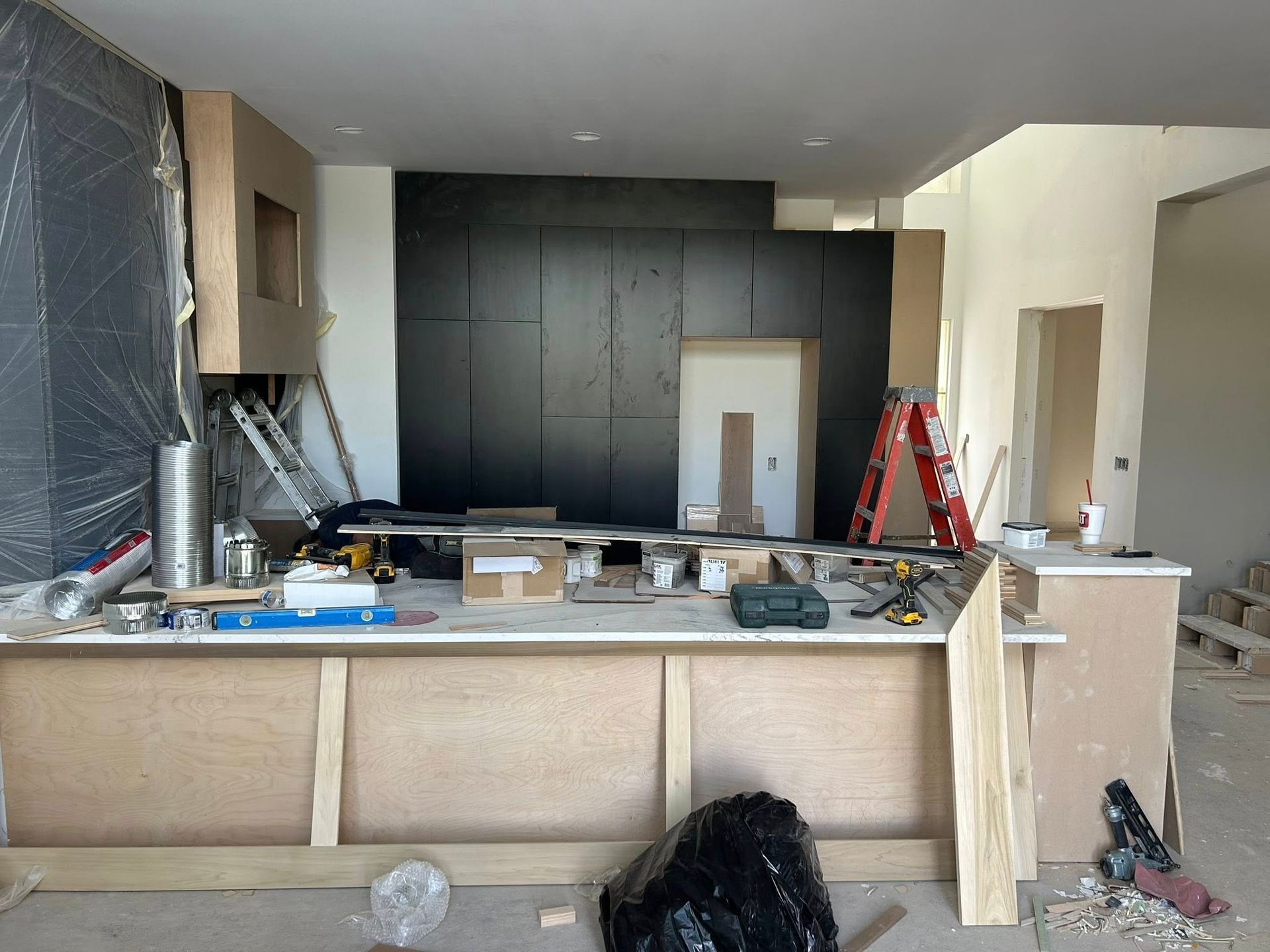 Kitchen renovation in progress: cabinetry, black accent wall, tools, ladders, and construction materials.