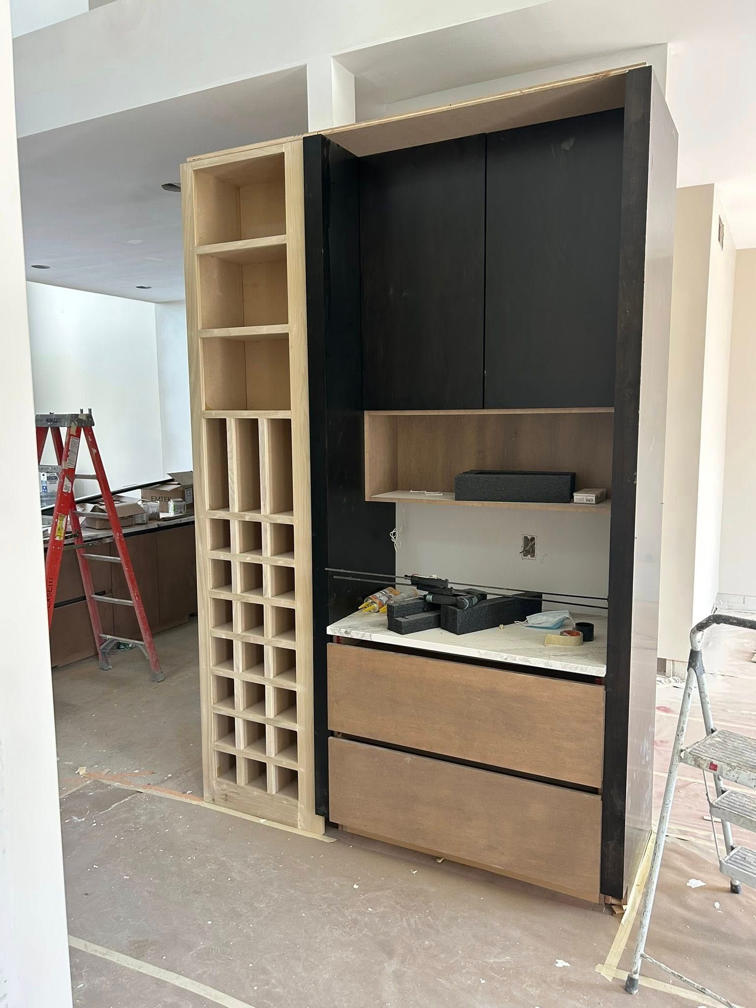 Wooden built-in cabinet being constructed with wine rack, drawers, and shelving. Interior renovation.