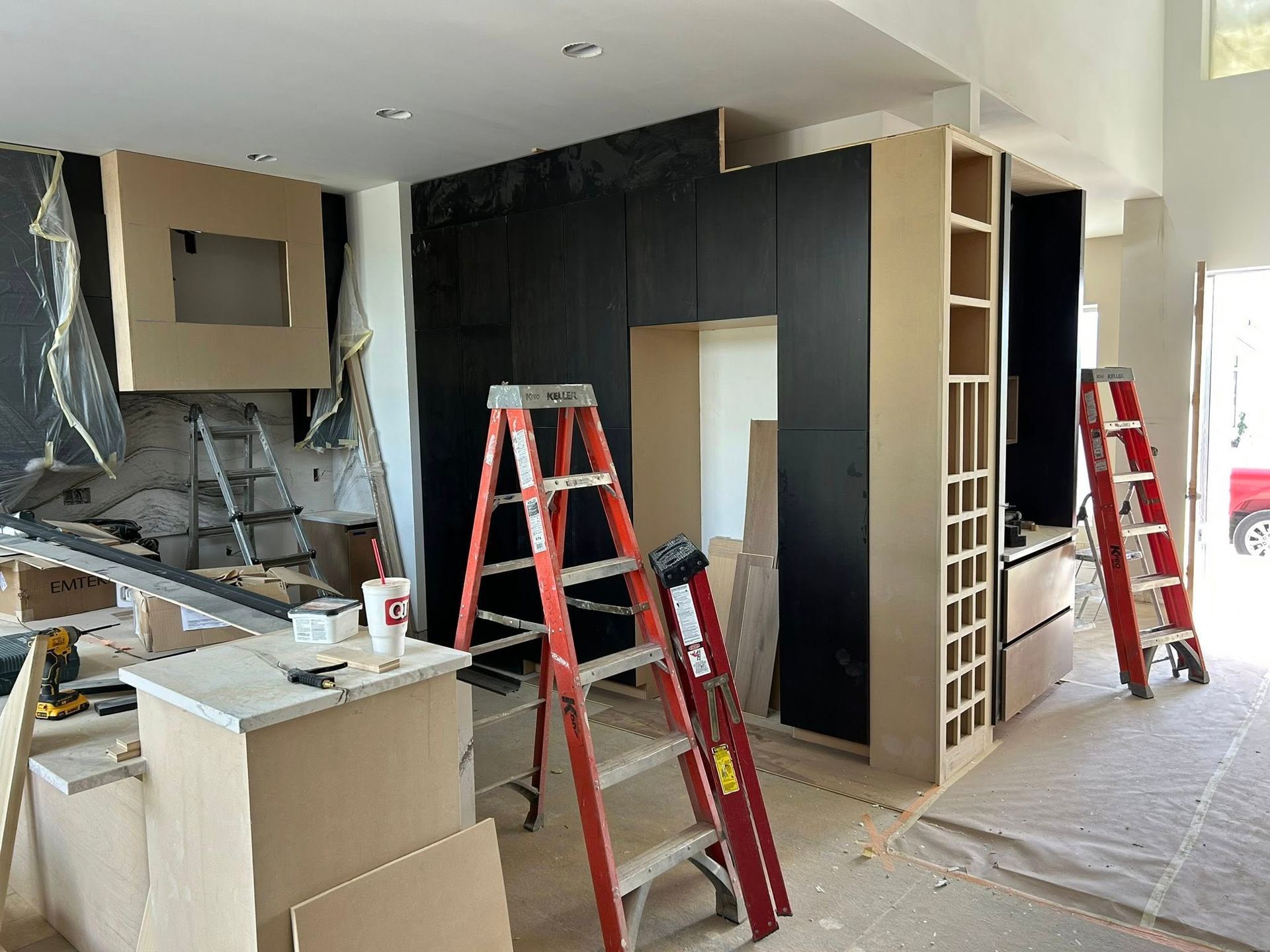 Kitchen remodel in progress, featuring unfinished cabinets, black wall, and two red ladders.