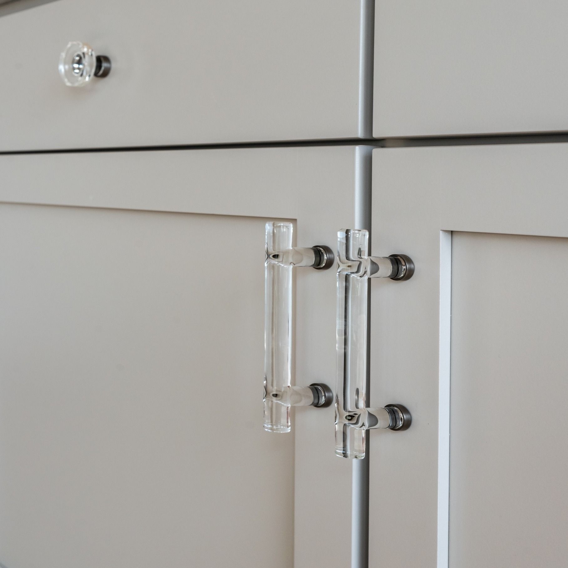 Close-up of light gray cabinet doors with clear acrylic pull handles and round knobs.