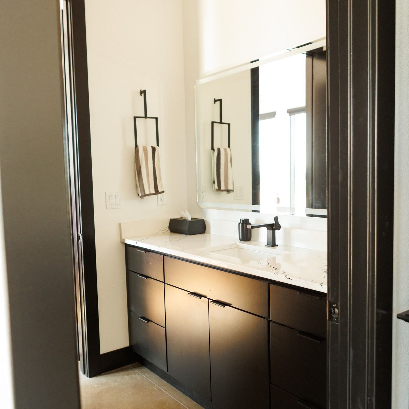 Bathroom with black cabinets, white countertop, large mirror, black faucet, and towel rack.