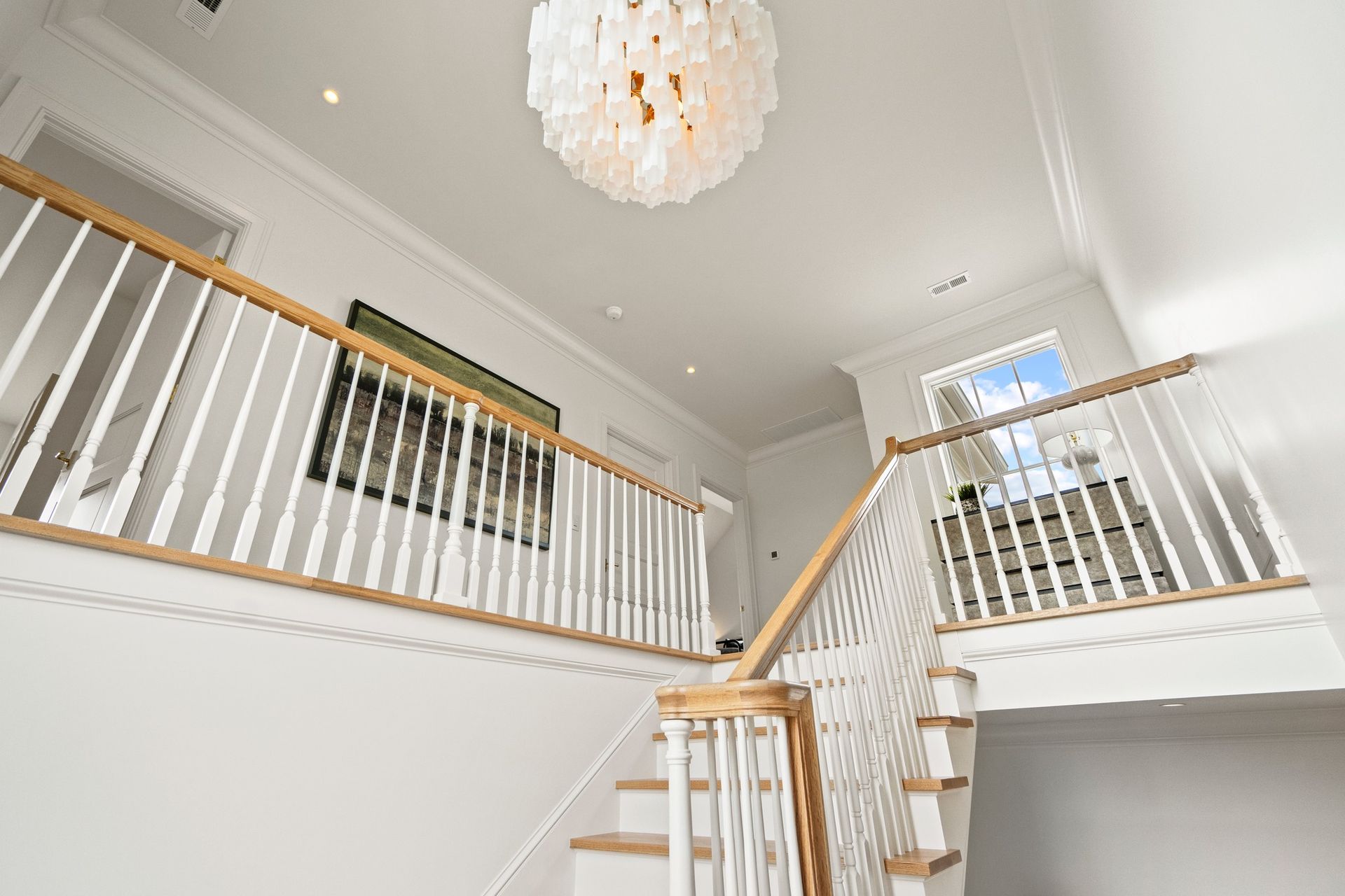 Bright indoor entryway with a wooden staircase, white railings, and a large, textured white orb chandelier overhead.