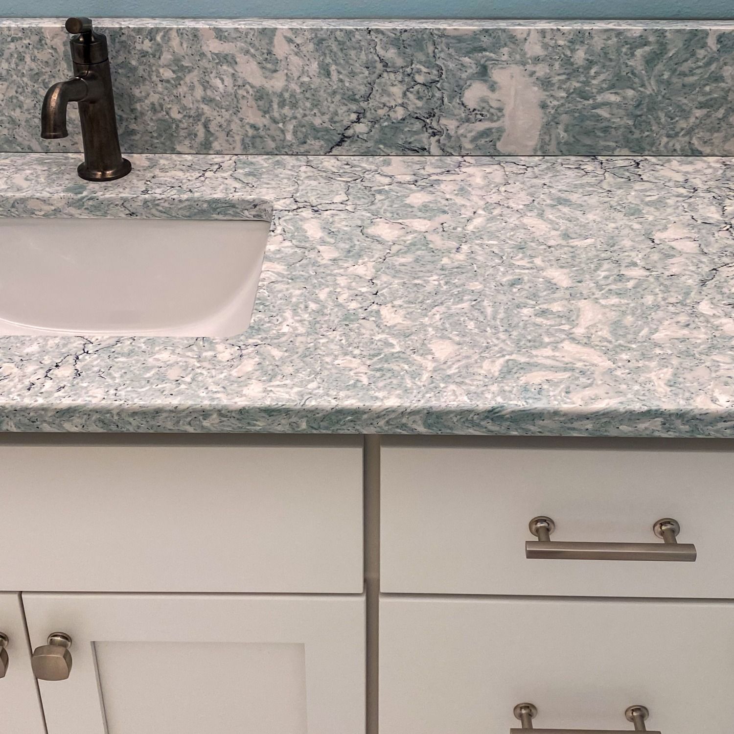 White bathroom vanity with light blue countertop, a sink, and dark faucet.
