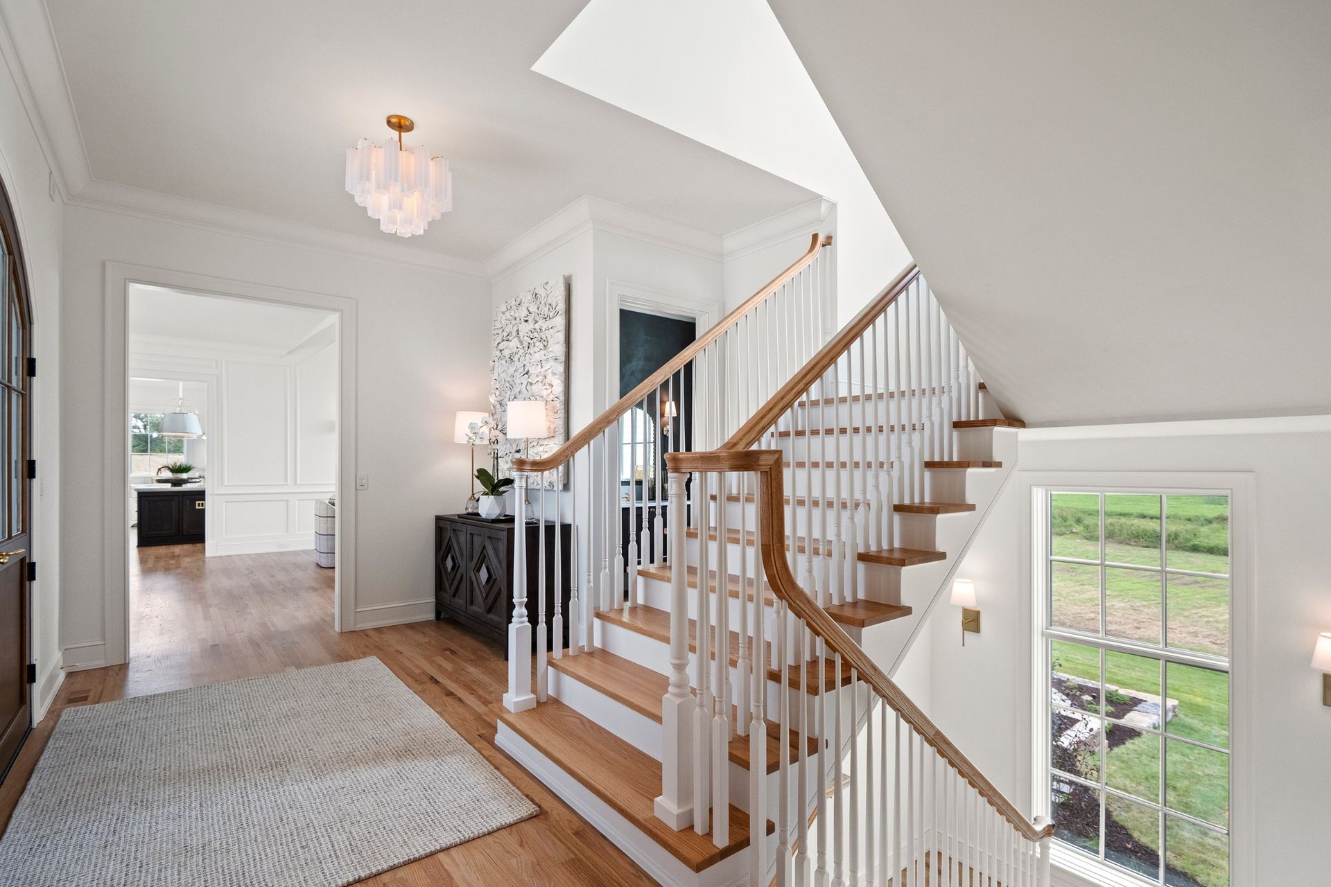 Bright, airy interior hallway with wooden staircase, white walls, and a fluffy rug.