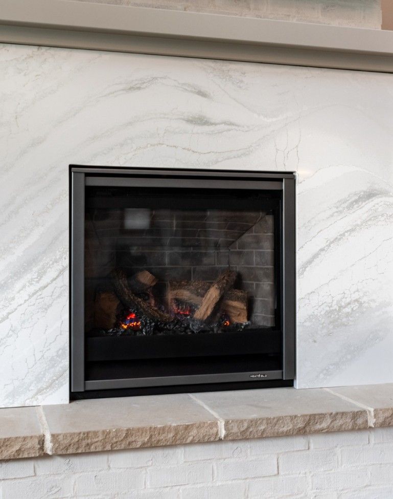 A fireplace with white-and-grey marble surround, black metal insert, and a tan stone hearth above white brick.
