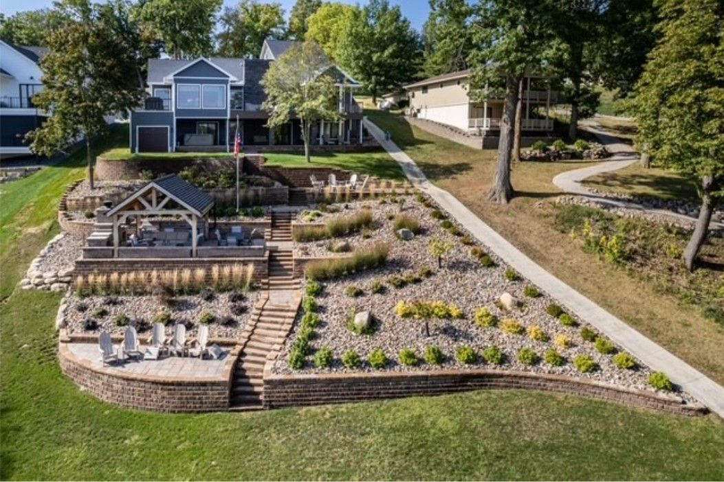 Terraced garden with flower beds and a greenhouse beside a lakeside house