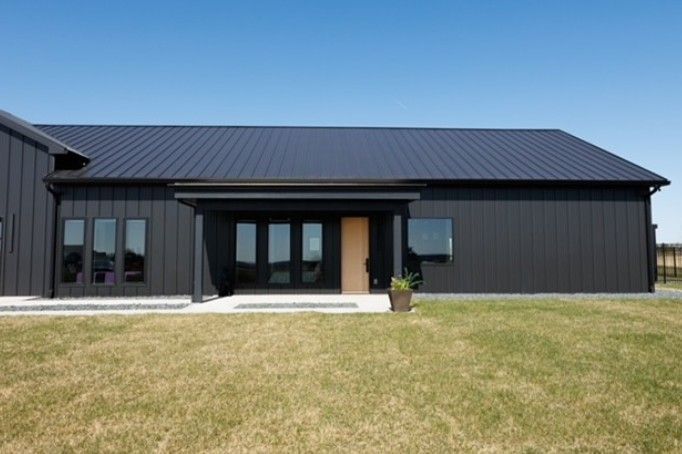 Modern black single-story house with a metal roof and a front lawn, centered entrance.