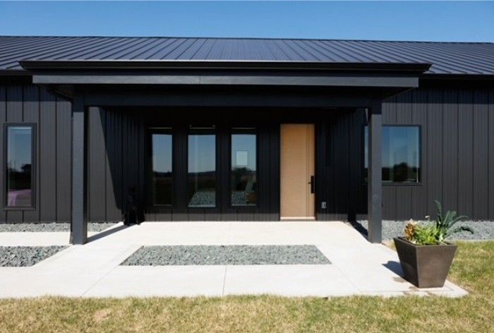 Modern black house exterior with large windows, covered entry, and concrete walkway leading to the front door