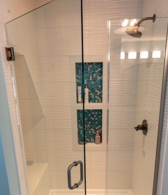 Glass shower enclosure with white blinds and teal decorative wall panels inside