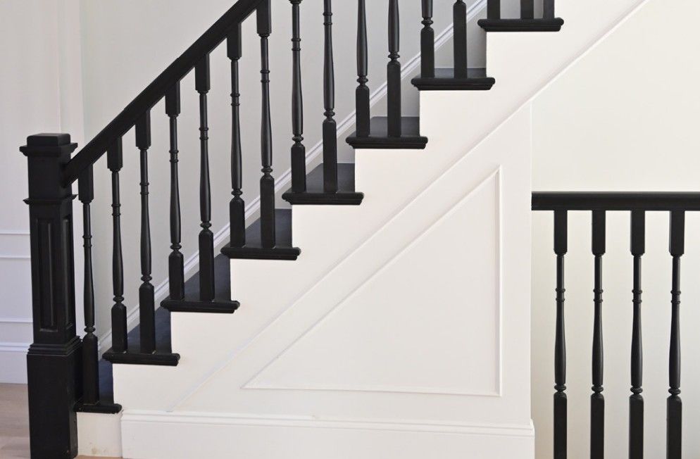 A staircase with black wooden spindles, railing, and treads against white walls and decorative trim.