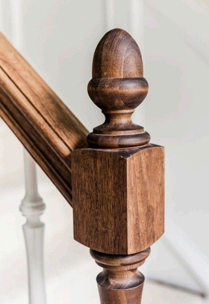 Close-up of a dark-stained wooden newel post with a decorative acorn-shaped finial at the top of a staircase.