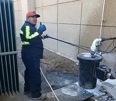 Man in work attire gives thumbs up while operating equipment near a building.
